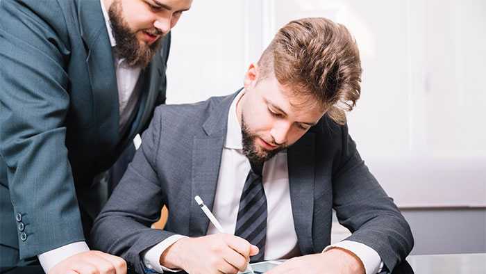 Boss standing over worker's shoulder watching him work