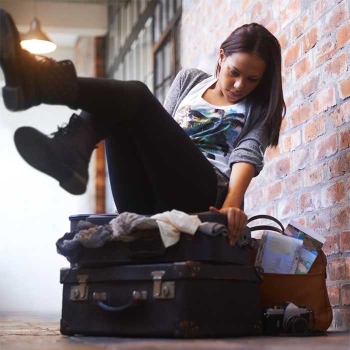 Girl falling onto a suitcase in an attempt to get it to close due to overstuffing