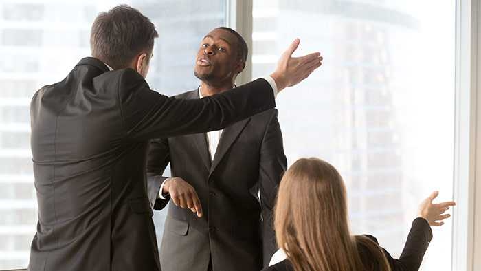 Two men in business suits standing in a meeting and gesture abrasively toward each other