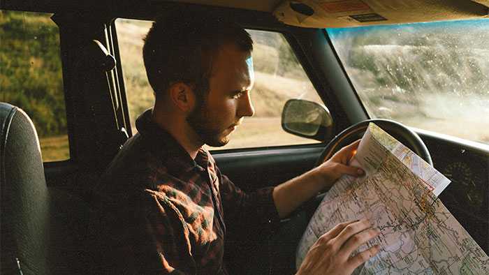 man in car thoughtfully examining an atlas
