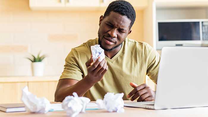 Man looks at paper wad in his hand with 3 more on his desk