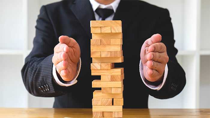 Hands blocking jenga blocks from falling