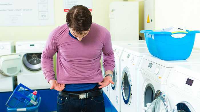 Guy putting on an obviously shrunken shirt at the laundromat