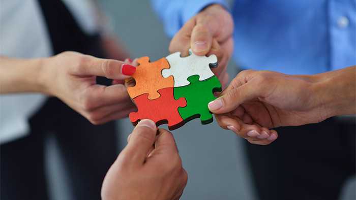 Four hands putting together wooden jigsaw pieces