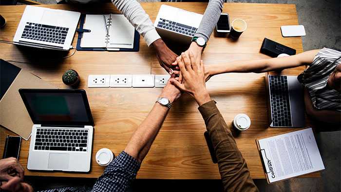 Scrum Team reaching across a shared table to do a hand stack