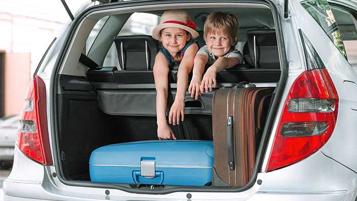 Two too happy kids in backseat of SUV look out the back hatch packed with suitcases