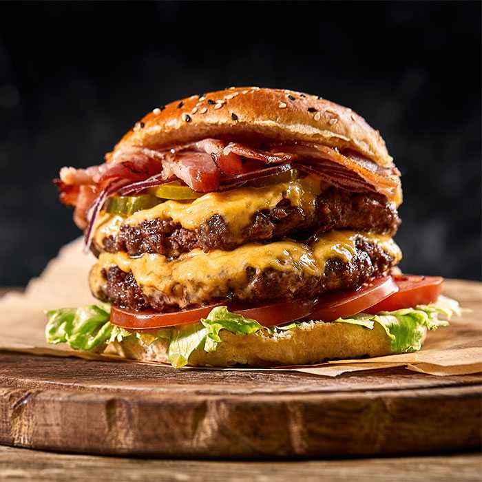 Towering double cheeseburger slathered with bacon and cheese containing thin slices of tomato