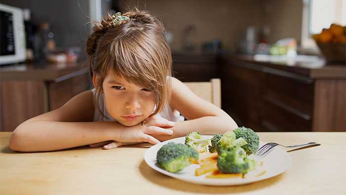 Girl staring at broccoli with hatred in her eyes