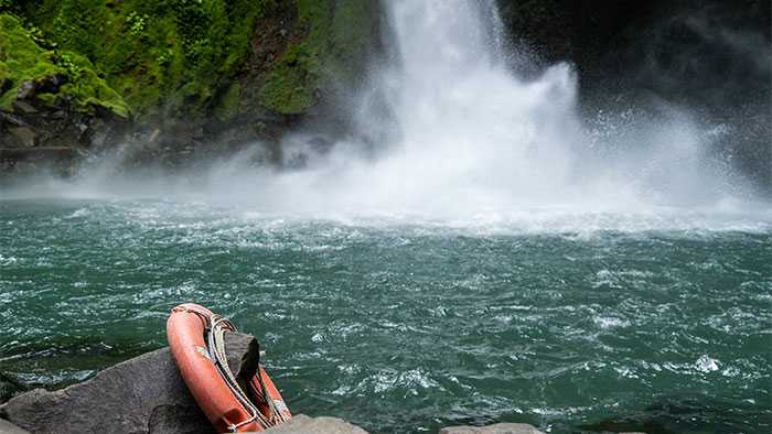 magnificent waterfall and lake surrounded by trees with a lifesaving tube hanging from a rock