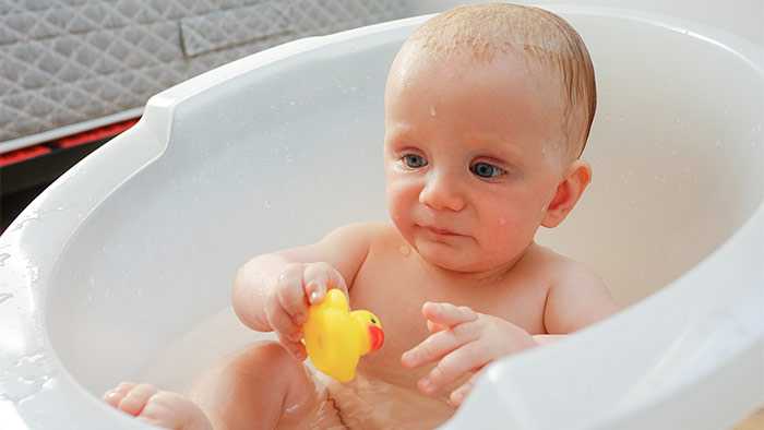 Baby sitting in bucket of water with rubber duckie