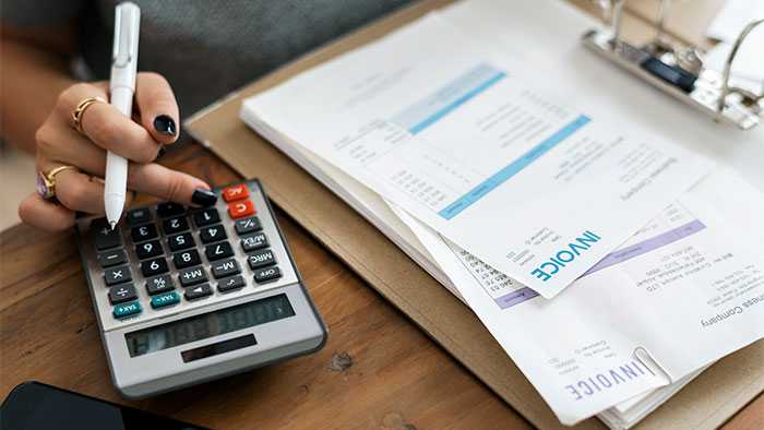 Woman's hand hovering over calculator next to stack of invoices