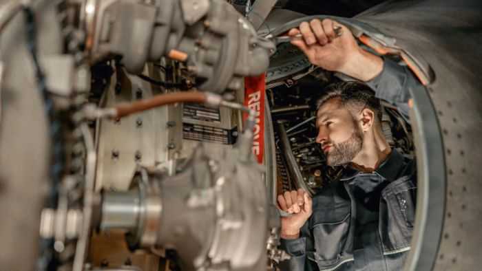 Airplane mechanic in the middle of plane parts tightening something with a wrench