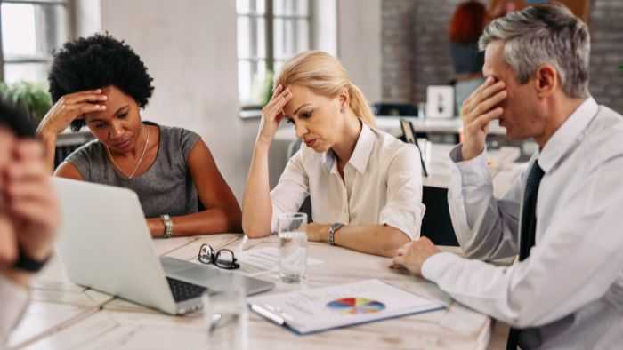 Three confused and frustrated co-workders sitting around a laptop struggling with a problem