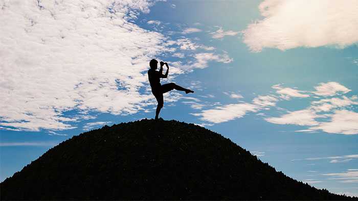 Silhouette of a man on a mountain practicing one-legged stand