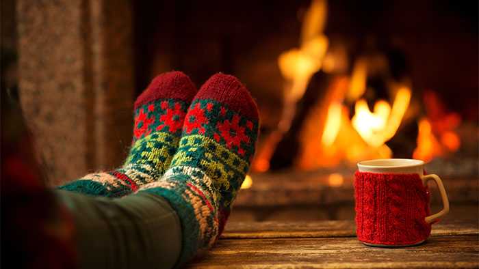 Socked feet proped up relaxing in front of fire next to hot chocolate mug