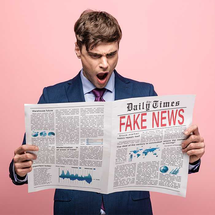 Guy staring incredulously at open news paper with fake news headline