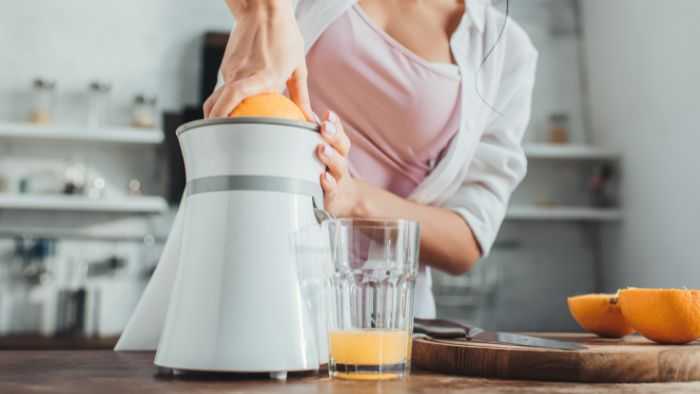 lady smashing an orange on a juicer and glass with very little juice